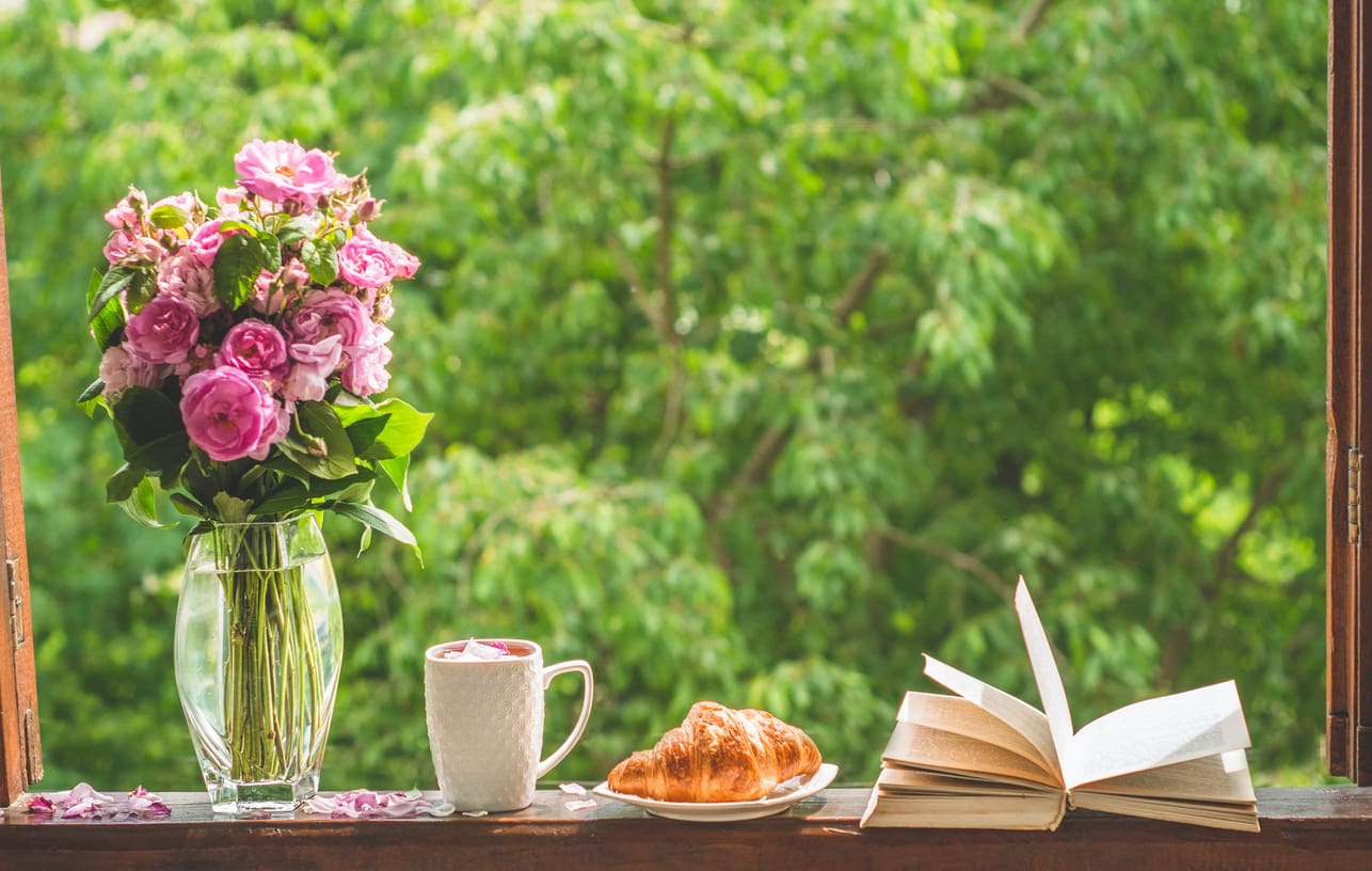 Book, croissant, cup of tea and roses on a wooden window. Read books. Romantic concept